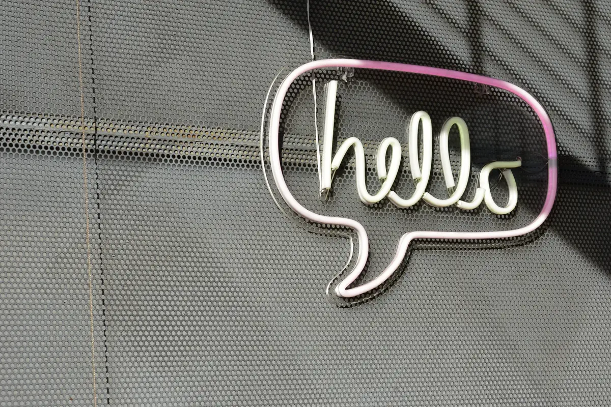 White and pink neon speech bubble reading “hello” on a perforated metal wall